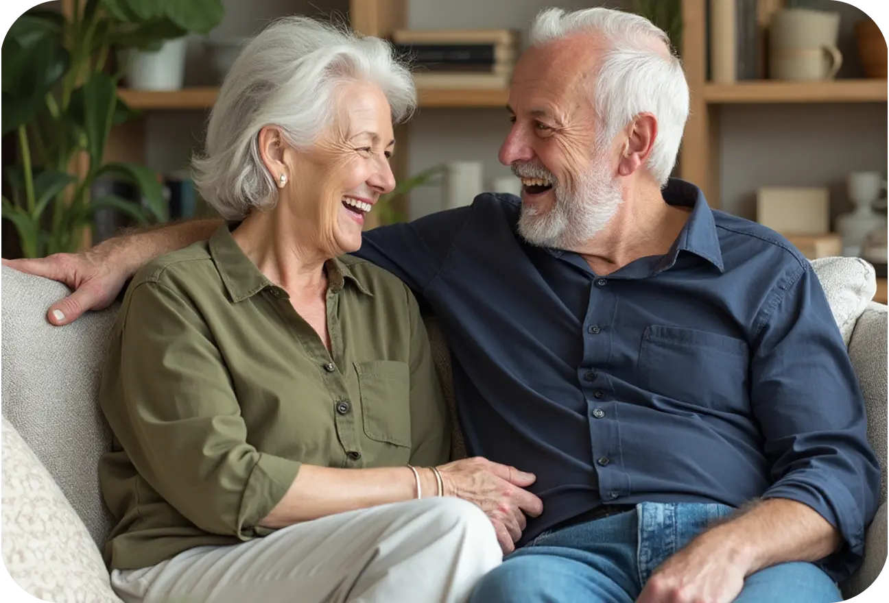Senior couple sitting together on a couch, smiling and laughing.