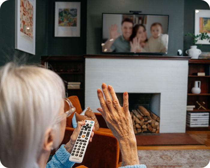 An elderly woman waving at the television on a video call on her tv with her family.