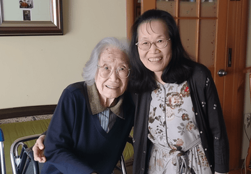 smiling adult daughter stands next to her elderly mother 