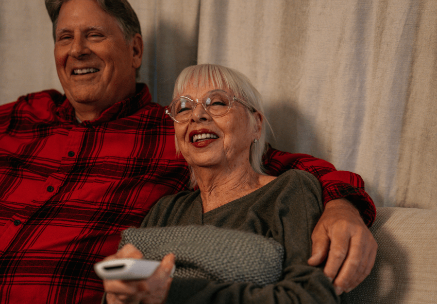 elderly couple smiling on the couch watching tv