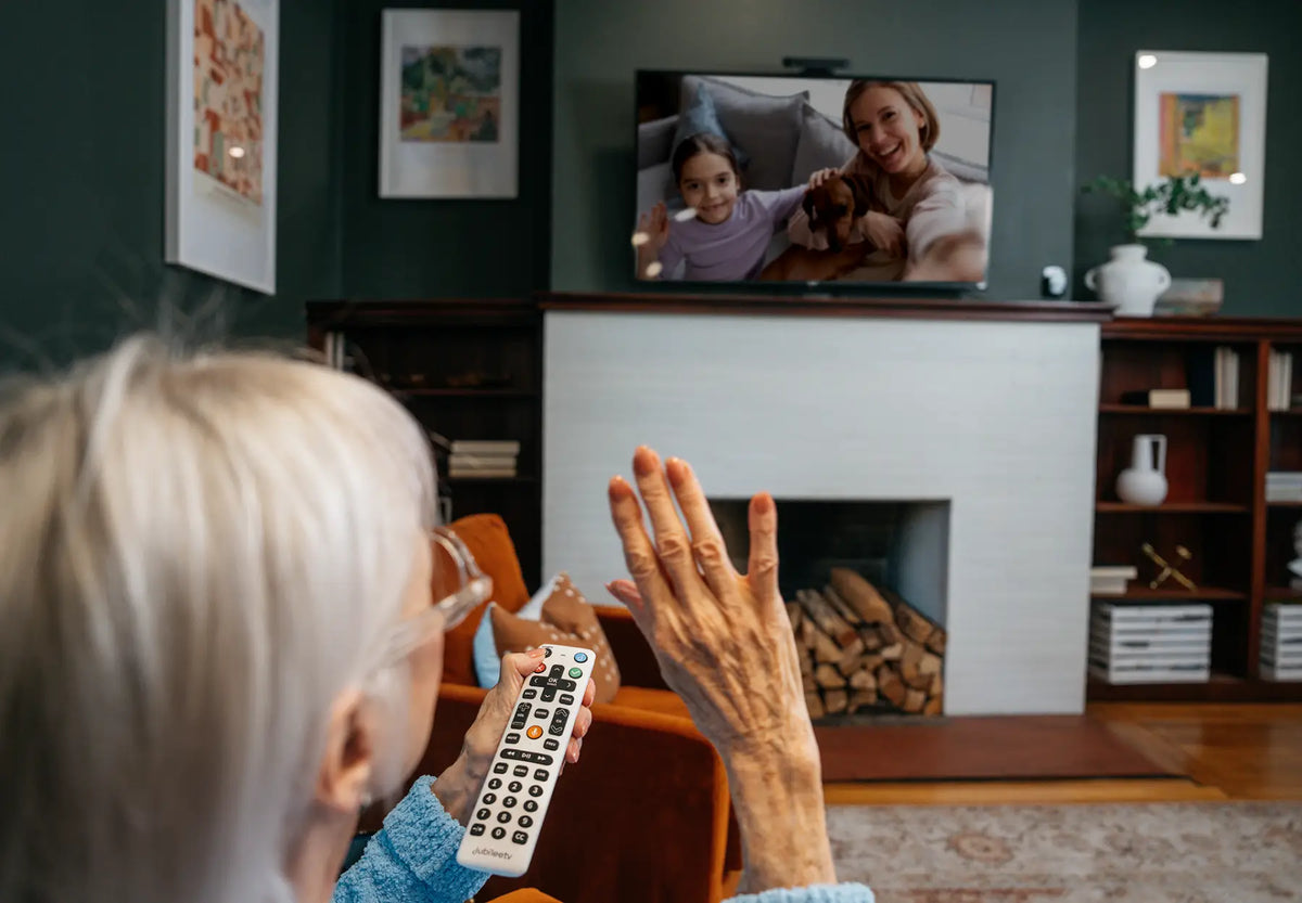elderly woman waving to loved ones for large screen video call 