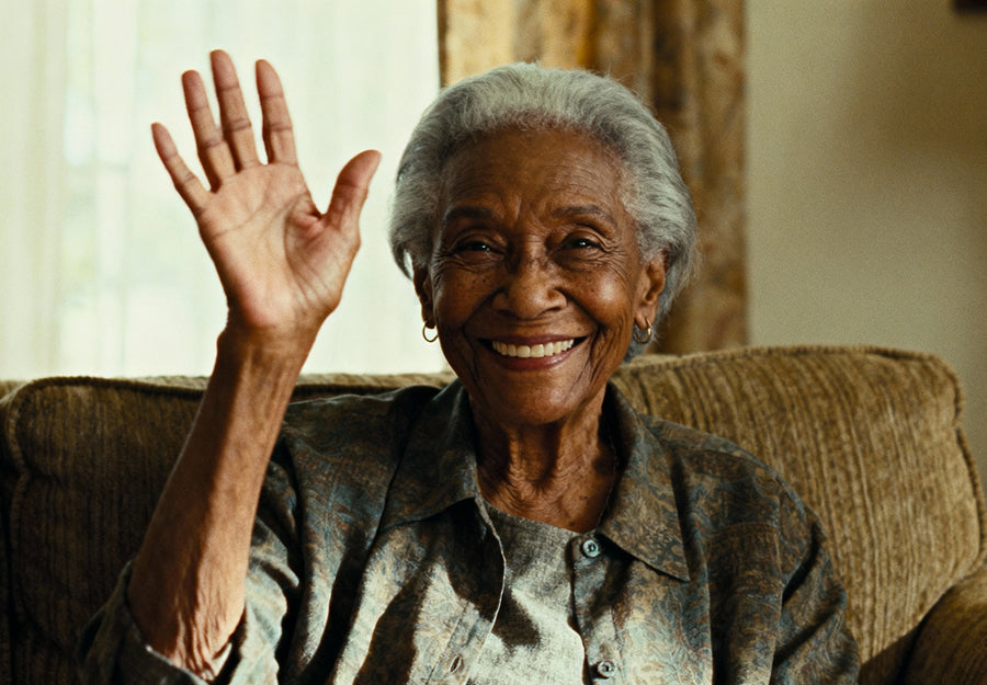 An elderly woman is waving during a TV video call