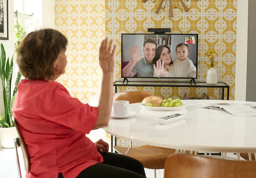 An elderly woman waving during a video call on TV