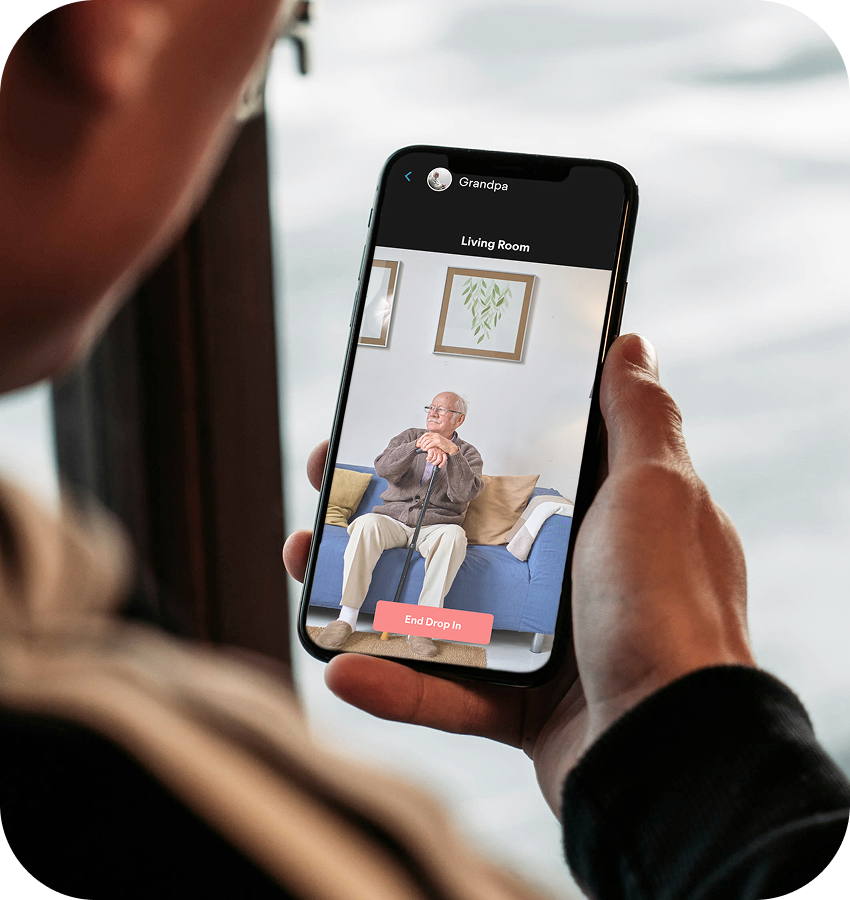 Person holding a smartphone with a quiet one-way video call to an elderly person on a couch.