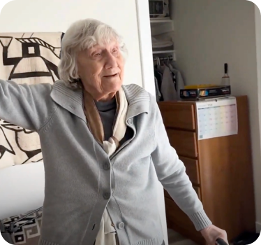 an elderly woman smiling and walking independently through her home with a cane.