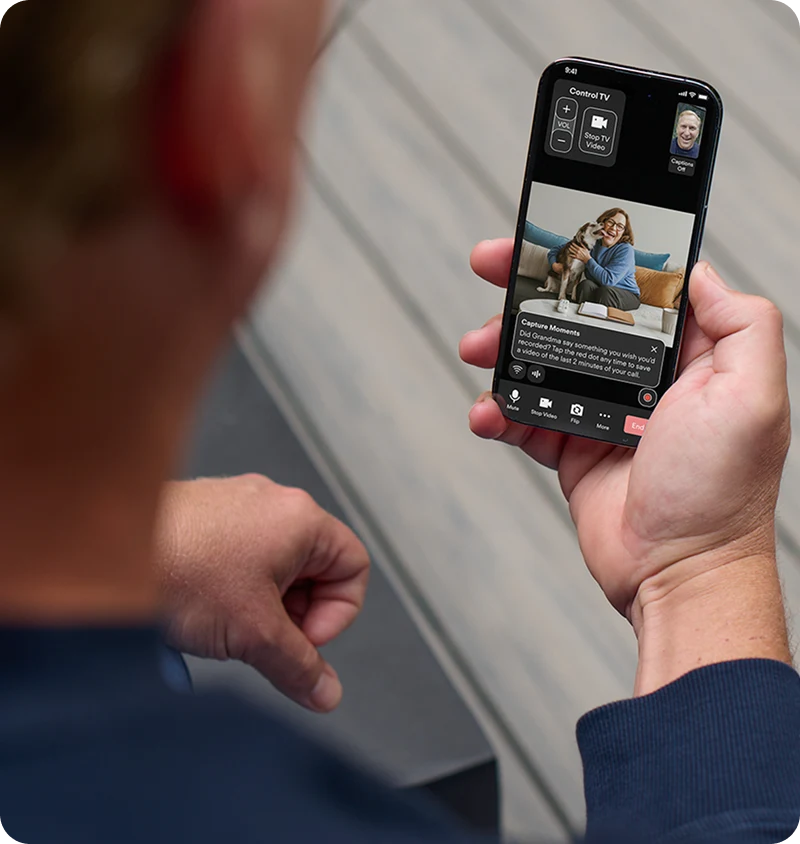 Man holding a smartphone displaying a video call with his elderly mom and her dog on a couch.