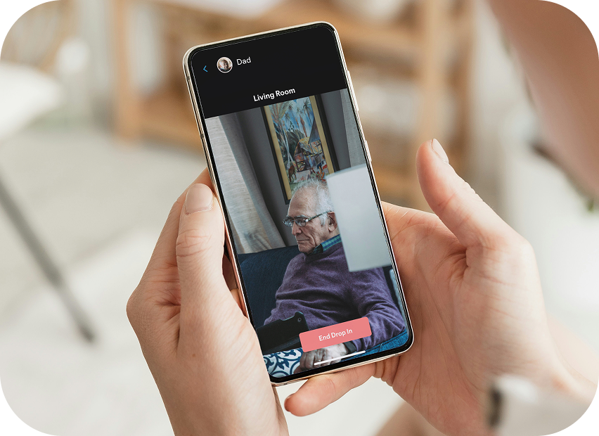 Person holding a smartphone with the JubileeTV app open and in quiet drop-in mode, showing an elderly person in a living room that has fallen asleep.
