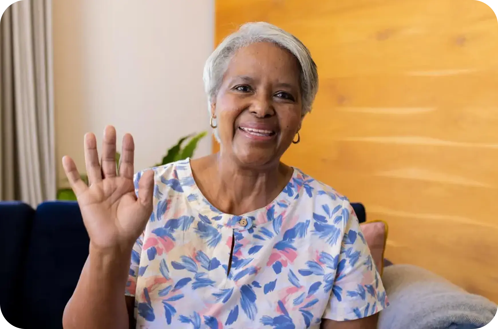 Woman waving at the camera indoors with a warm background