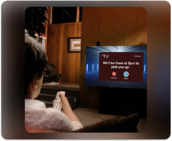 A woman pictured at the edge of the frame of the photograph watching TV with a JubileeTV remote in her hand, receiving a reminder that someone is picking her up at 3pm.
