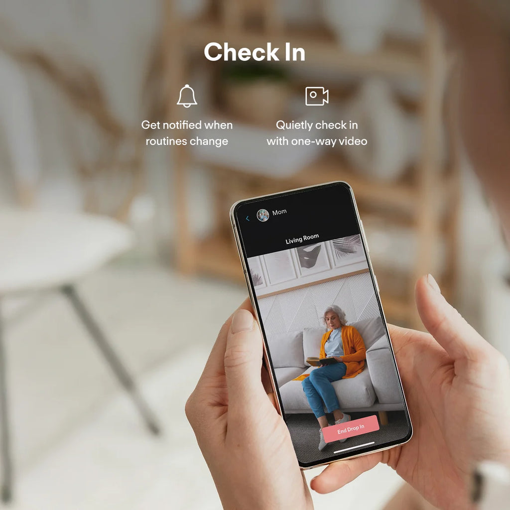 Person using a smartphone app for elderly monitoring device feature in a living room setting.