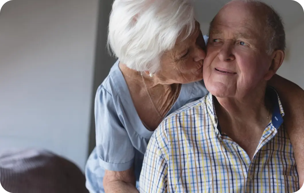 elderly woman kissing her husband with dementia on the cheek